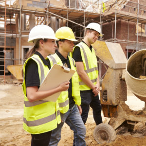 Builder Using Cement Mixer On Building Site With Apprentices